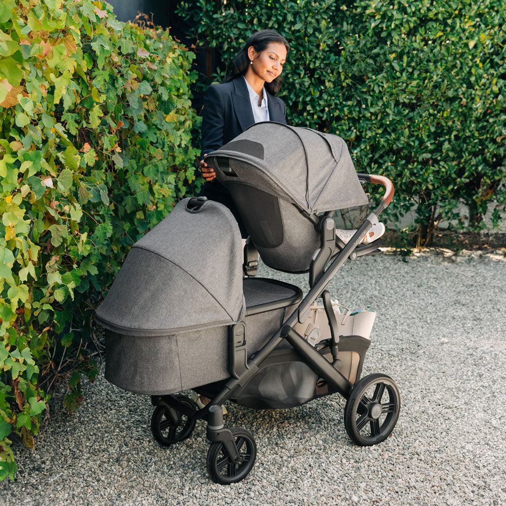 Woman pushes baby in UPPAbaby Bassinet V3 - GREYSON (Charcoal Melange) and toddler in toddler seat