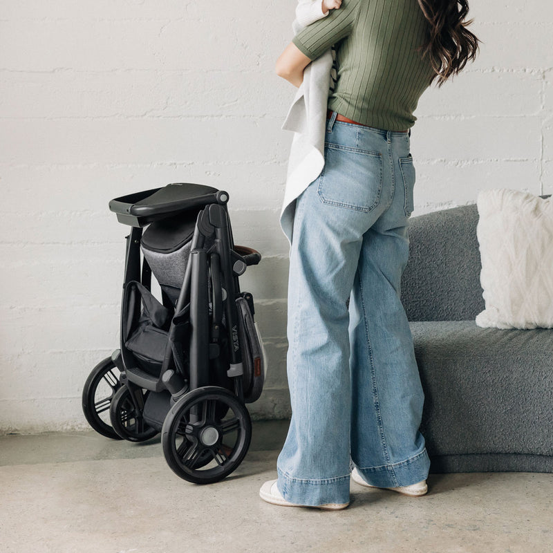 Mom holds baby while standing next to folded UPPAbaby VISTA V3 Stroller - GREYSON (Charcoal Melange)