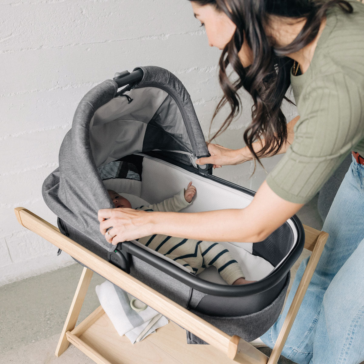 Mom adjusts canopy for baby lying in bassinet attached to UPPAbaby New Bassinet Stand - Natural