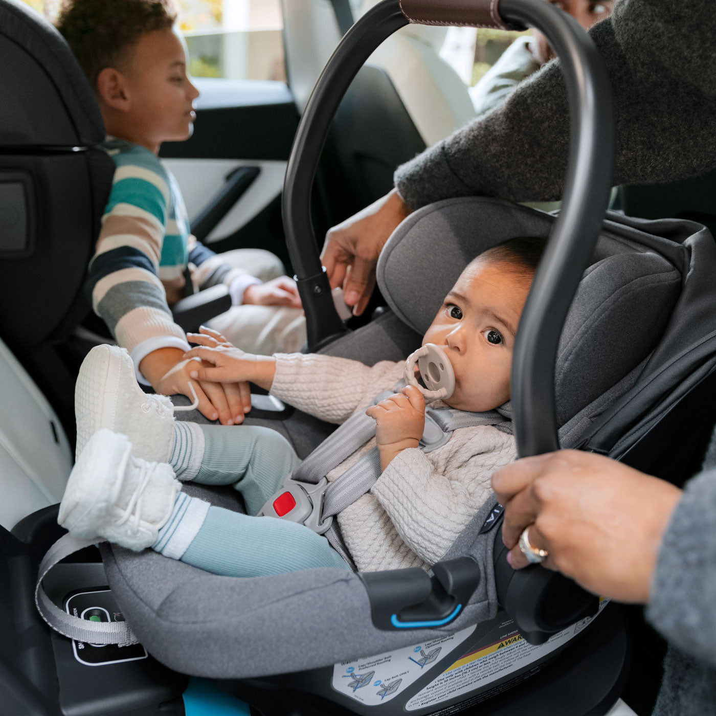 Baby in UPPAbaby ARIA Infant Car Seat - GREYSON (Dark Grey) holds brothers hand