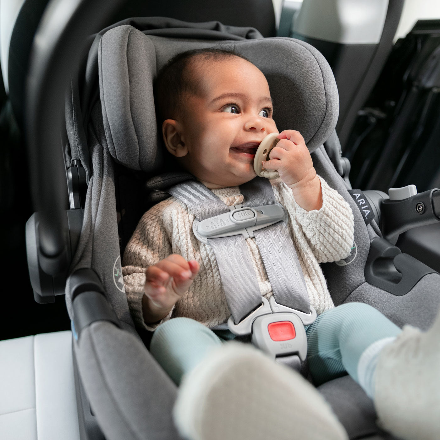 Baby smiles riding in UPPAbaby ARIA Infant Car Seat - GREYSON (Dark Grey)