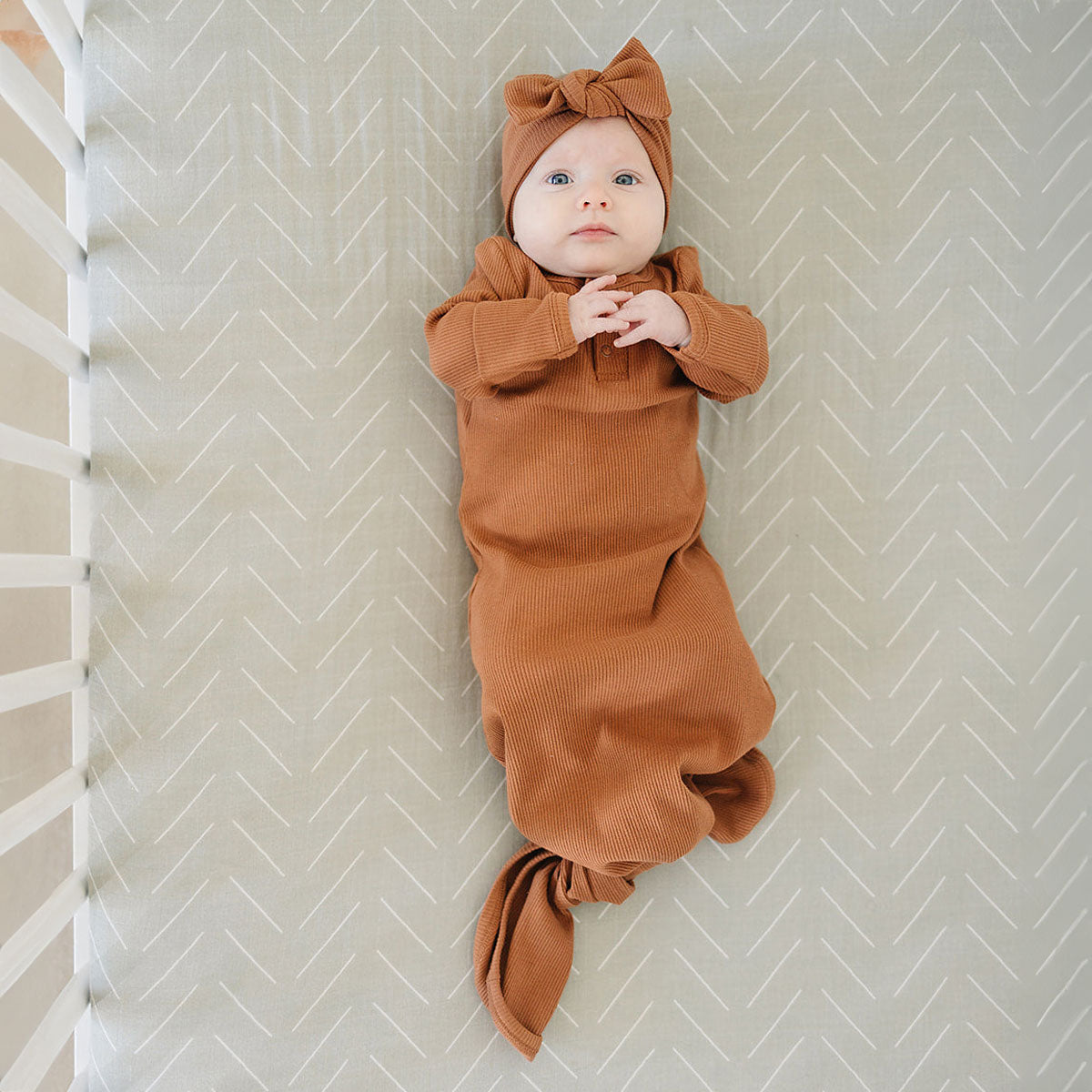 Baby girl lying in crib wearing Mebie Baby Organic Cotton Ribbed Knot Gown - Rust