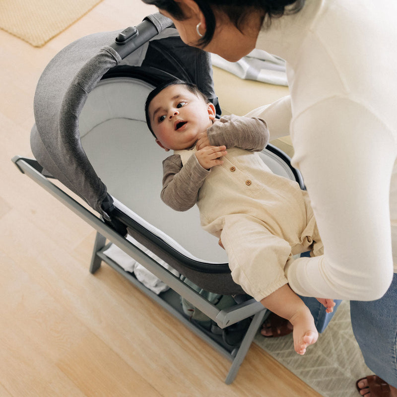 Mom places baby into bassinet attached to UPPAbaby New Bassinet Stand - Grey