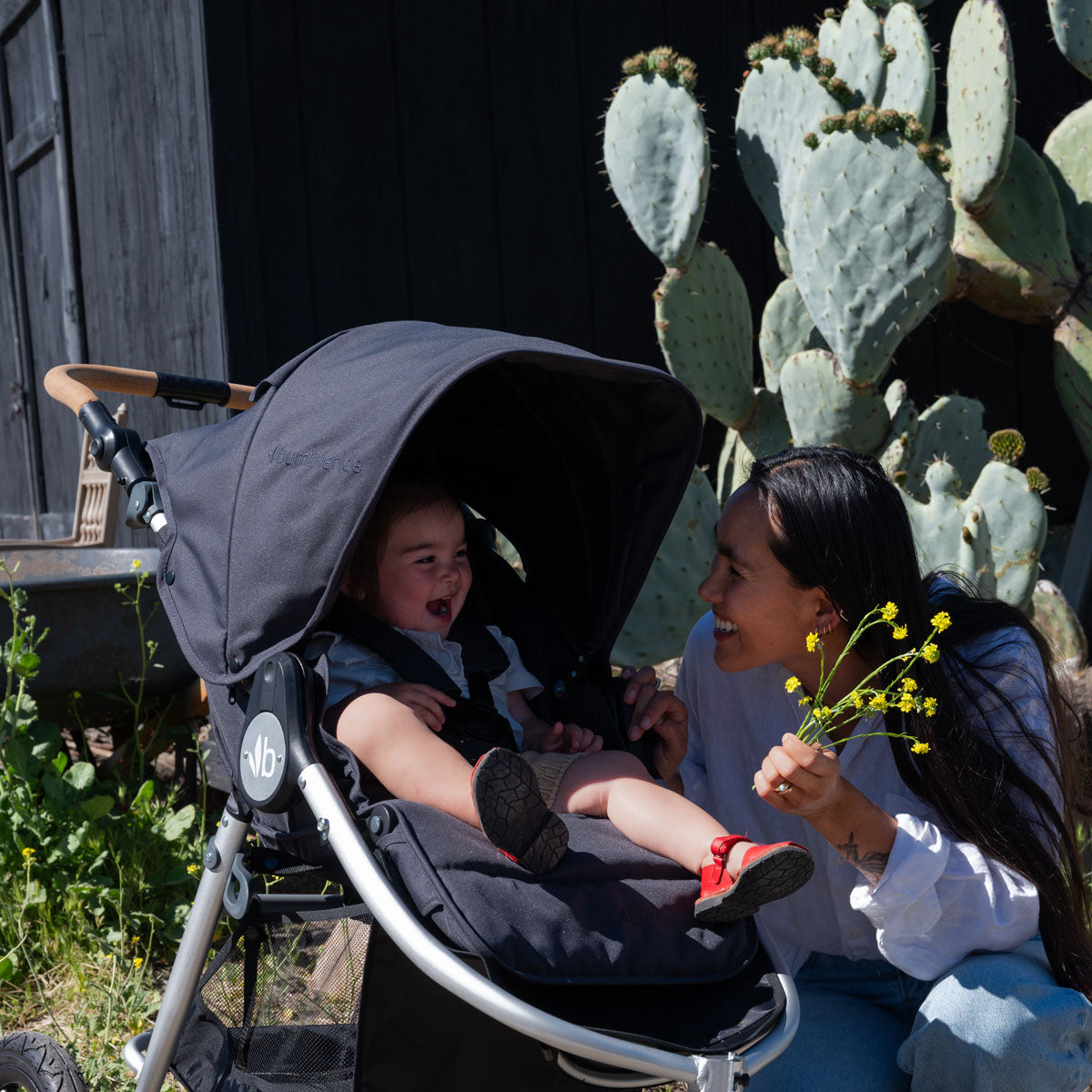 Mom holding flowers smiles at little girl sitting in Bumbleride 2024 Indie All Terrain Stroller - Dusk