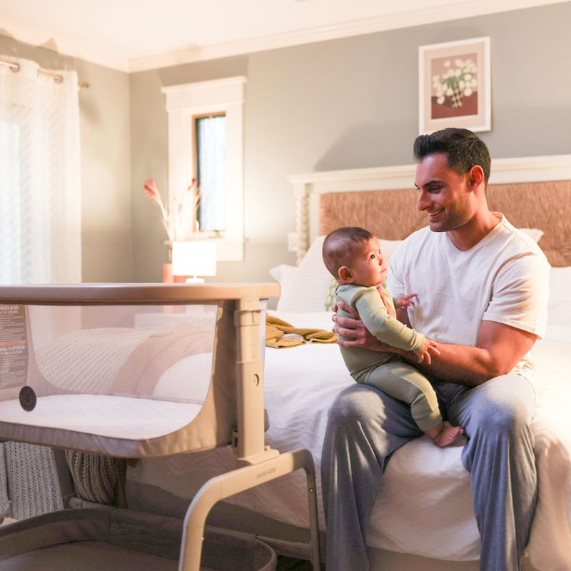 Dad and baby next to Maxi-Cosi Iora Bedside Bassinet - Classic Oat