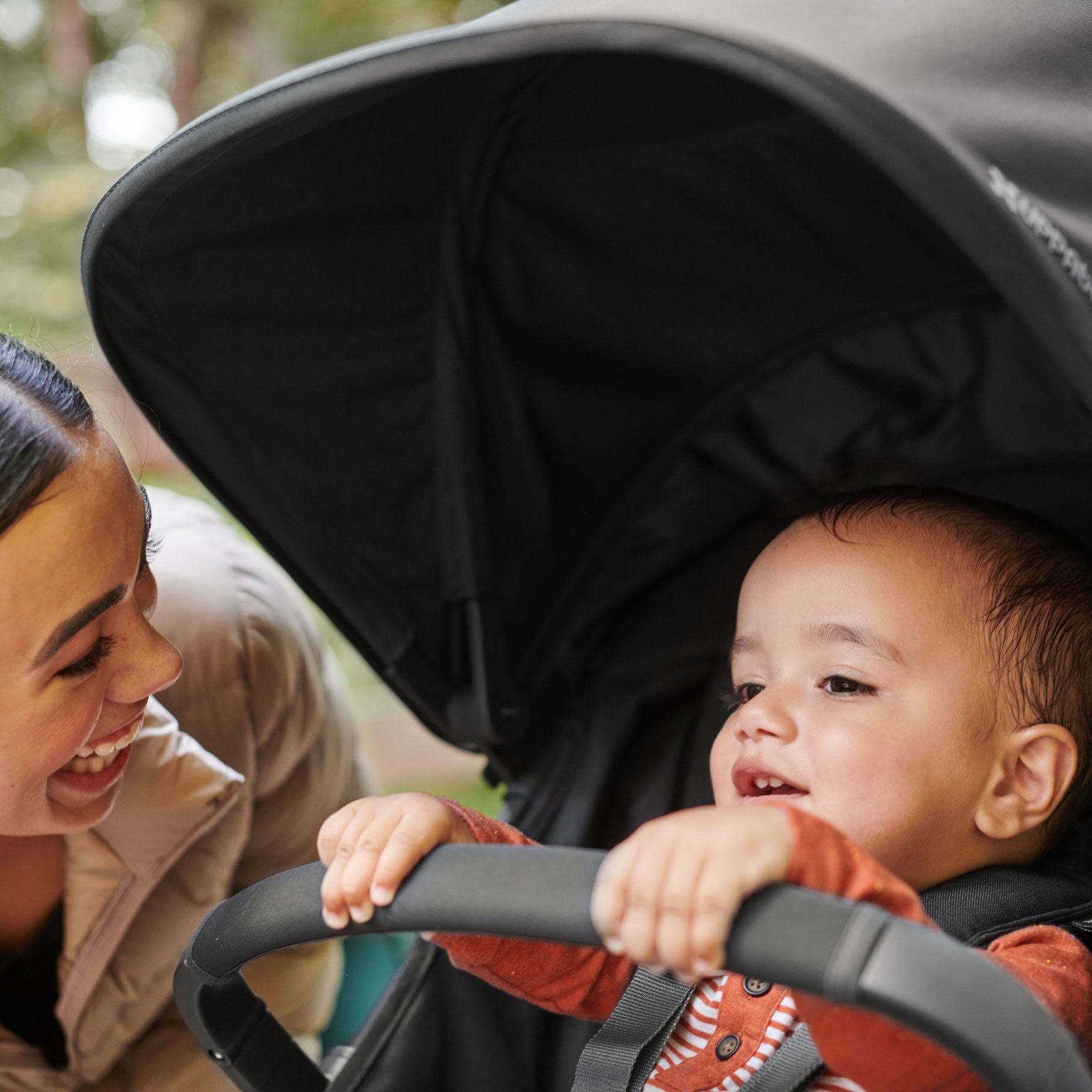 Mom smiles at baby sitting in RIDGE stroller with attached UPPAbaby RIDGE Bumper Bar