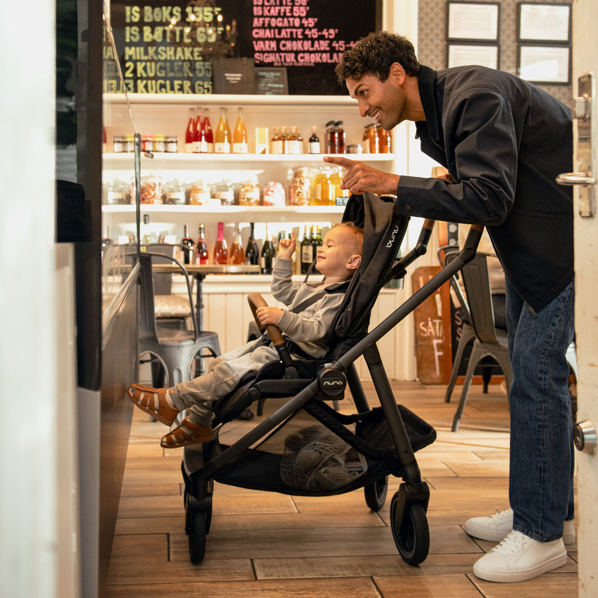 Man ordering at cafe while pushing child in Nuna SWIV Stroller - Caviar