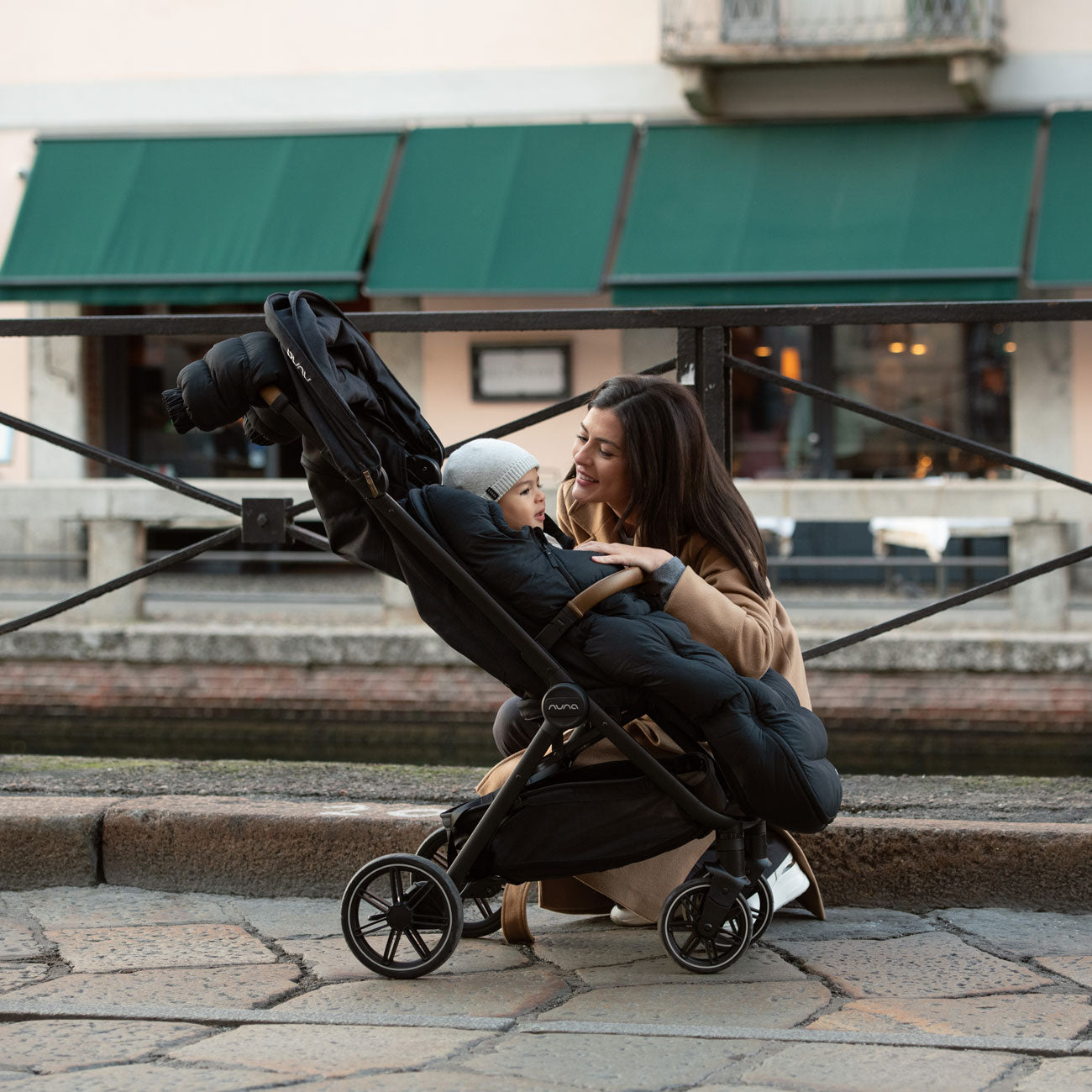 Mom kneeling next to toddler riding in Nuna TRVL LX Stroller - Caviar