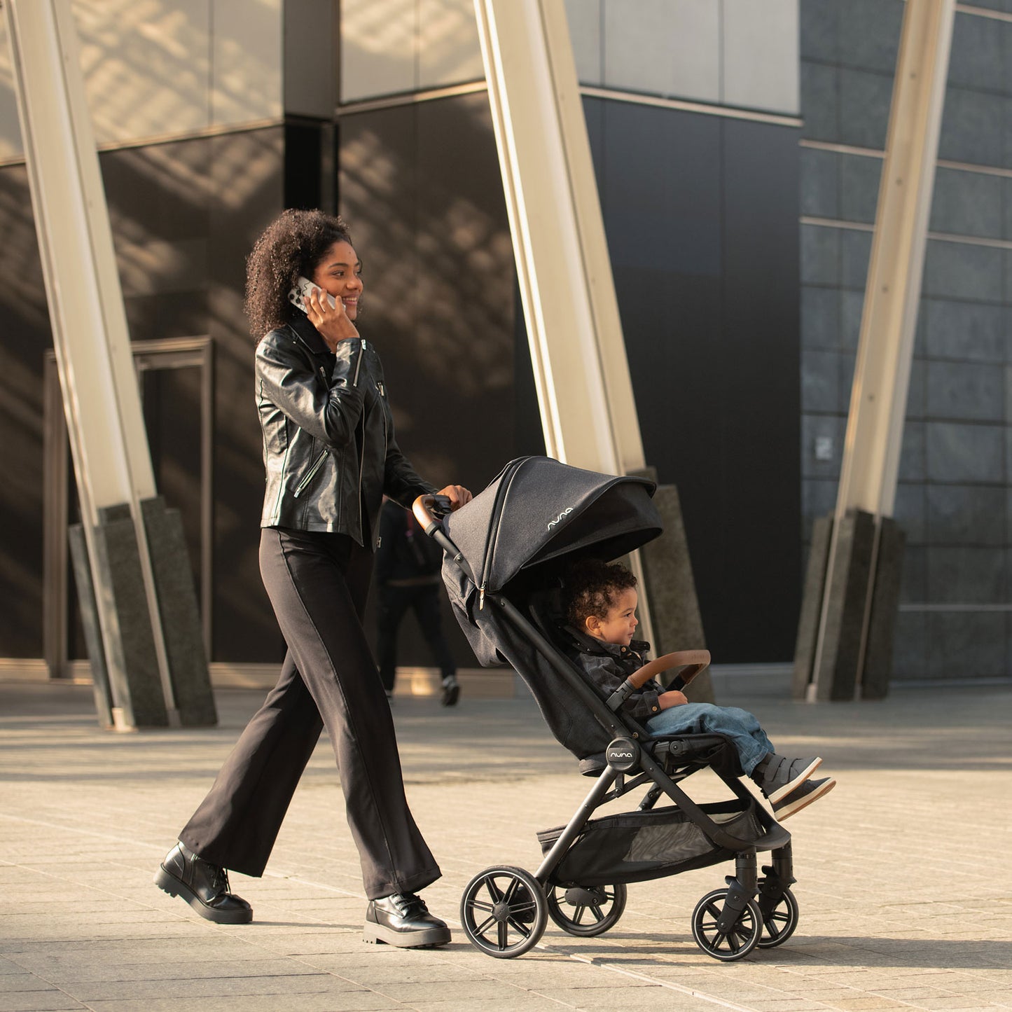 Mom talks on phone while pushing toddler in Nuna TRVL LX Stroller - Caviar