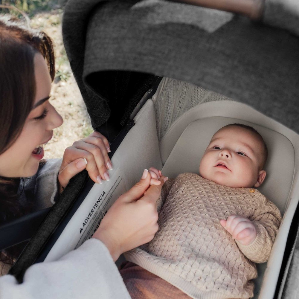 Mom smiles at baby lying in Romer Sera Bassinet - Peppercorn