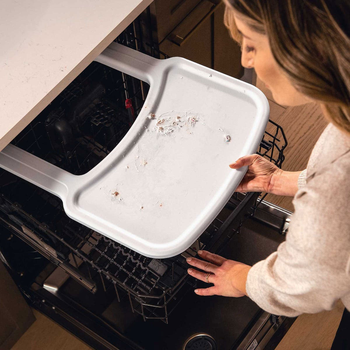 Mom places tray of Nuna ZAAZ High Chair with MagneTech Secure Snap - Carbon in the dishwasher