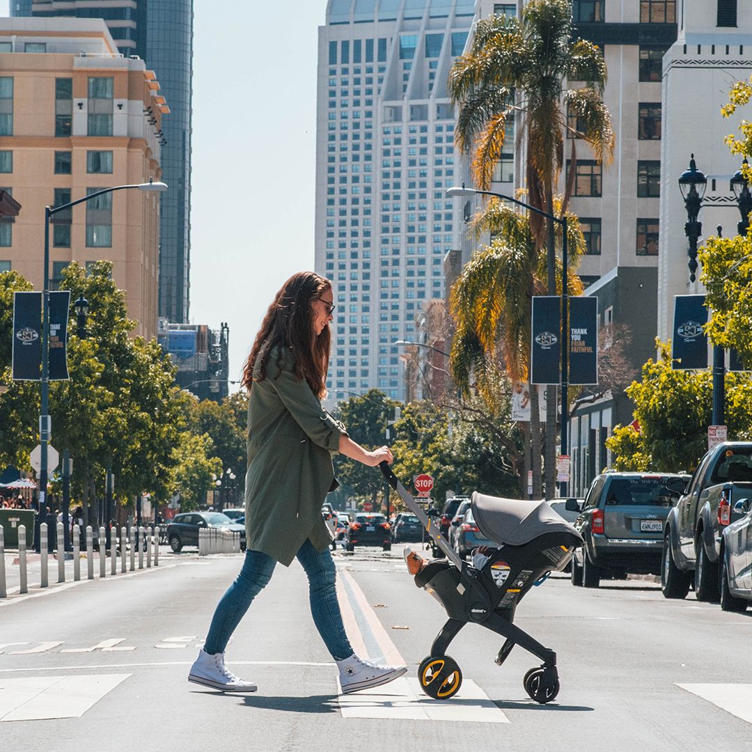 Mom pushes Doona Infant Car Seat and Stroller on city street