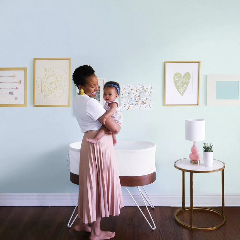 Mother holds baby next to Happiest Baby SNOO Smart Sleeper - White